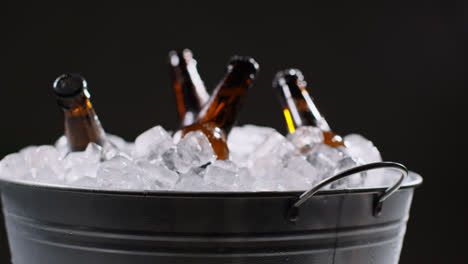 Nahaufnahme-Von-Glasflaschen-Mit-Kaltem-Bier-Oder-Alkoholfreien-Getränken,-Die-In-Einem-Mit-Eis-Gefüllten-Eimer-Vor-Schwarzem-Hintergrund-Kühlen